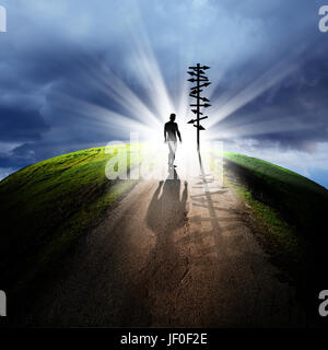 Imagen conceptual de siluetas de hombre y signo direccional en carretera vacía sobre el cielo nublado con haz de luz Foto de stock
