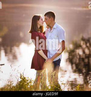 Retrato de una hermosa pareja joven en amor y besos de pie cerca del río. Foto de stock