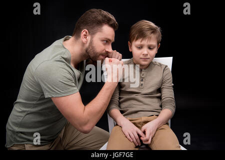 Enojado padre amenazante y hacer gestos miedo pequeño hijo sentado en una silla, problemas familiares concepto