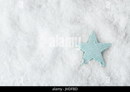 Fotografía cenital de una estrella de madera azul pálido sobre fondo blanco de nieve artificial con copia espacio a la izquierda. Fondo de Navidad.
