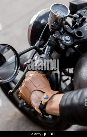 Cierre de hipster biker chico mano en guante piel mantenga el control del acelerador de estilo clásico cafe racer Moto custom en vintage garaje Fotografía de stock -