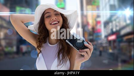 Compuesta Digital de la milenaria mujer en verano sombrero con cámara frente a la calle borrosa con bengalas y bokeh Foto de stock