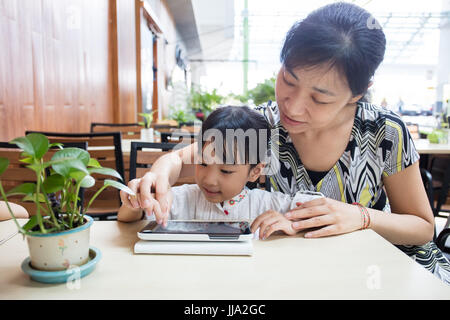 Chino Asia niña jugando tablet pc con su madre en la cafetería al aire libre