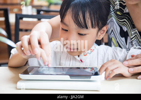Chino Asia niña jugando tablet pc con su madre en la cafetería al aire libre