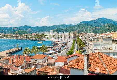 Vista de ciudad costera con azulejos de color naranja de los tejados en primer plano y hermosas montañas verdes con el cielo azul de fondo, Marmaris, Turquía Foto de stock