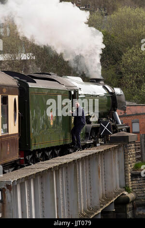Conductor sube en la icónica locomotora a vapor, el motor A3 60103 Clase LNER Flying Scotsman, resoplando humo - Keighley & Worth Valley Railway, Inglaterra, Reino Unido. Foto de stock