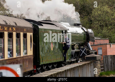 Conductor sube en la icónica locomotora a vapor, el motor A3 60103 Clase LNER Flying Scotsman, resoplando humo - Keighley & Worth Valley Railway, Inglaterra, Reino Unido. Foto de stock
