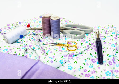 Una selección de accesorios de costura, como tijeras, algodón, con tejido normal y patrón aparece sobre fondo blanco.