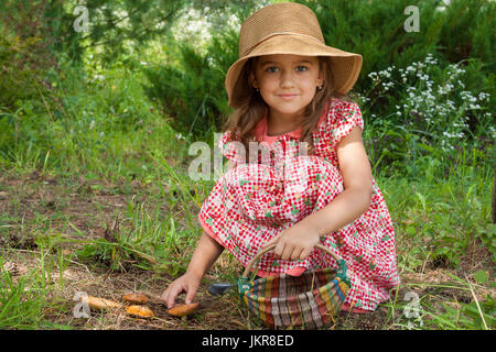 Adorable pequeño de seis años de edad, niña rusa en canasta de mimbre con sombrero en mano encantados de setas suillus, Semi-sentada y mirando a la cámara W
