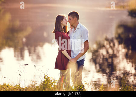 Retrato de una hermosa pareja joven en amor y besos de pie cerca del río. Foto de stock