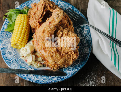 Mazada pollo frito con maíz y ensalada de papa sobre la superficie de madera