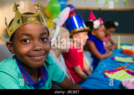 Retrato de niño sonriente luciendo corona con amigos en el fondo durante la fiesta Foto de stock