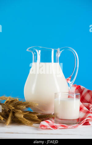 Vista cercana de leche orgánica fresca en el vaso y la jarra con espigas de trigo sobre la mesa de madera Foto de stock