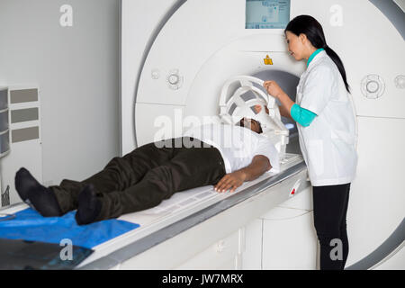 Doctora mascarilla de fijación al paciente varón tumbado en la resonancia magnética en el hospital de la máquina Foto de stock
