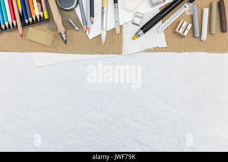 Suministros de dibujo diferente en el escritorio: lápices multicolores, diversos pinceles, tizas, sacapuntas, cortador de papel Foto de stock