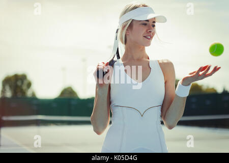 Sonriente joven jugador de tenis femenino la celebración de raqueta de tenis y pelota de tenis en la cancha de tenis Foto de stock