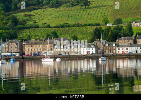 Waterfront edificios de la ciudad de Port Bannatyne refleja en aguas tranquilas de Harbor, en la isla de Bute, Escocia con el verde de las granjas en la colina detrás de la ciudad Foto de stock