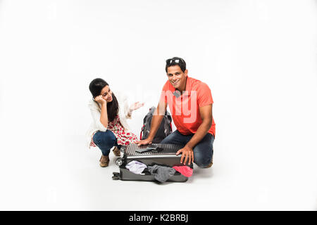 Fotos de pareja joven indio embalaje para vacaciones, intentando cerrar la maleta llena de ropa, sentados aislado sobre fondo blanco.