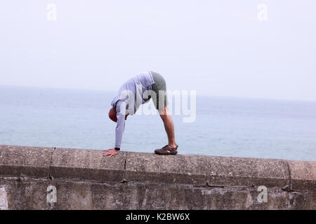 Hombre de 50 años, haciendo una pose de yoga perro boca abajo sobre la escollera en Cromer, Norfolk, Reino Unido.