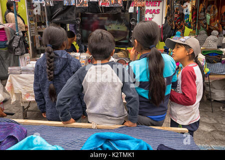 Abril 29, 2017 en Otavalo, Ecuador: niños indígenas quechuas viendo la televisión en la calle en el mercado del sábado