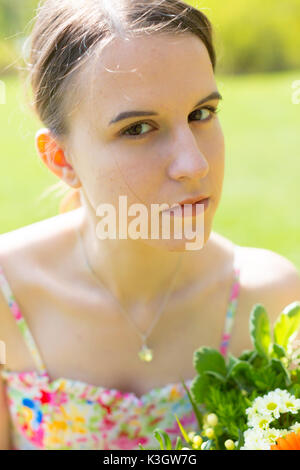 Lindo retrato de una mujer joven con un ramo de flores en un parque de verano. Outdoor retrato de una niña morena con pelo largo en la naturaleza Foto de stock