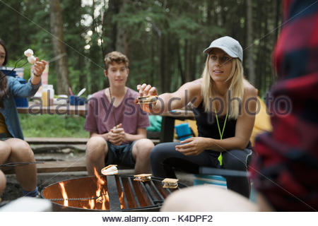 Profesora de adolescentes y estudiantes de la escuela al aire libre haciendo smores en camping fogata