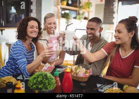 Feliz jóvenes amigos elevando las bebidas mientras está sentado a la mesa en la cafetería.