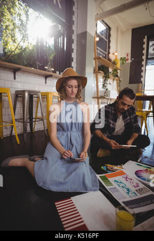Los jóvenes profesionales mediante tecnologías mientras está sentado con hojas en el suelo en la cafetería Foto de stock