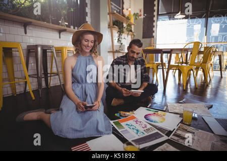 Jóvenes profesionales creativos utilizando tecnologías mientras está sentado con hojas en el suelo en la cafetería Foto de stock