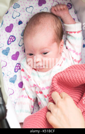 Despertar el bebé recién nacido en el pesebre, mirando la cámara con los ojos bien abiertos , madre poniendo la mano encima de su manta Foto de stock