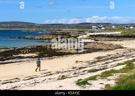 Hombre caminando el perro en la playa en la bahía cerca de Ballyconneely Mannin en Connemara, Condado de Galway, República de Irlanda