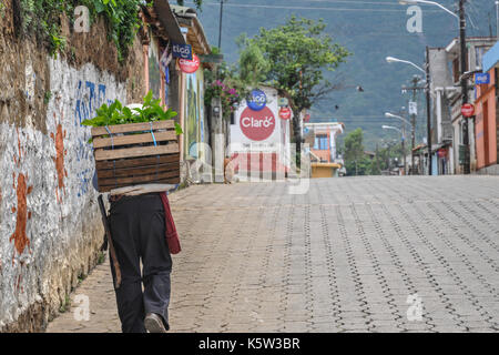 Hombre caminando en una calle en una calle vacía Un pueblo de Guatemala cerca del lago Atitlán con una caja de verduras frescas en la espalda