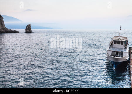 Viajar a Crimea - vista del barco amarrado cerca de nido de golondrina castillo en gaspra distrito y parus (vela) rock en la costa sur de Crimea del mar Negro en vísperas Foto de stock