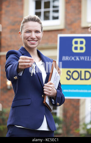 Realtor hembra de pie fuera de la propiedad residencial sosteniendo llaves