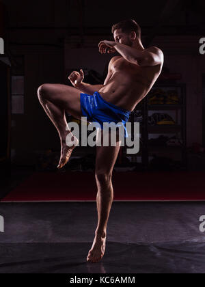 Un macho de MMA fighter formación patadas y puñetazos en un gimnasio oscuro Foto de stock