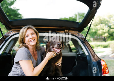 Retrato de mujer acariciando labrador retriever en el maletero del coche