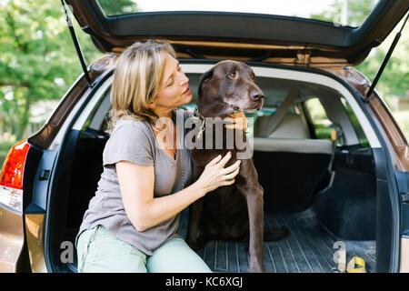 Mujer acariciando labrador retriever en el maletero del coche