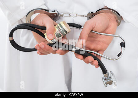 Close-up de un doctor manos sosteniendo los billetes de banco y esposas Foto de stock
