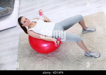 Ejercicio mujer con levantamiento de pesas en bola en casa salón Foto de stock