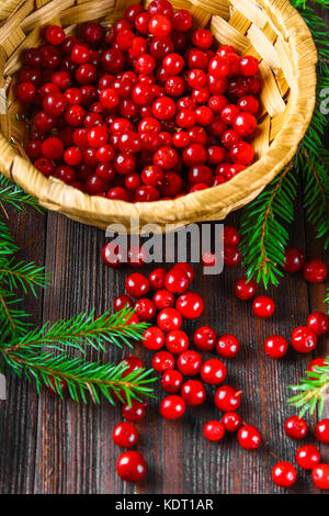 Cowberry, foxberry, arándano, Arándano rojo sorbos de la cesta sobre una tabla de madera marrón. rodeado de ramas de abeto.