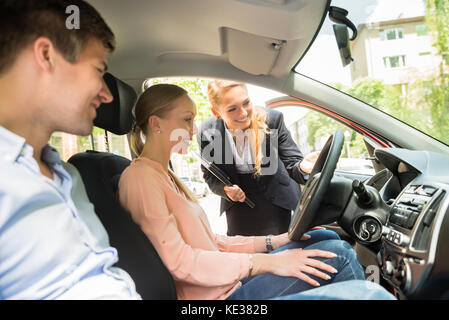 Feliz hembra joven vendedora que muestra un nuevo coche para par Foto de stock