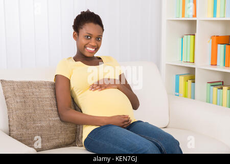 Feliz mujer embarazada sentada en un sofá en casa