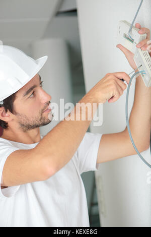 Electricista joven instalando dispositivo eléctrico en la pared Foto de stock