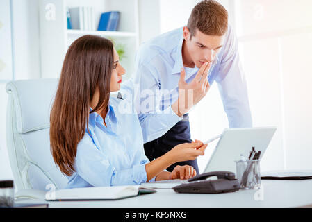 Dos jóvenes empresarios hablando en la oficina. Mujer sentada en un escritorio de oficina, de pie detrás de ella un joven hombre mirando el portátil. Foto de stock