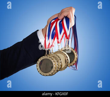 Primer plano de la mano del empresario celebración medallas sobre fondo azul. Foto de stock