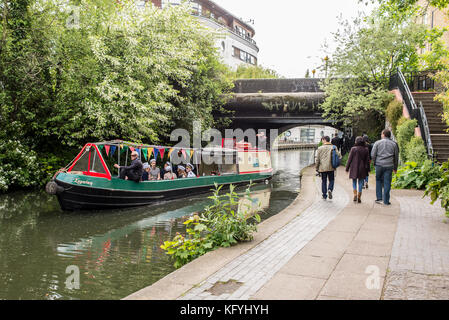 Narrowboat o barcaza pasando sobre el Regents Canal con gente caminando en el camino de sirga canalside cerca de la ciudad de Camden, Londres, Inglaterra, Reino Unido. Foto de stock