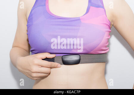 Mujer joven en el sujetador deportivo y monitor de ritmo cardíaco con cinta aislado en blanco Foto de stock