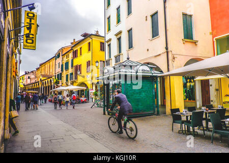 La vida cotidiana en Italia. Un hombre de negocios en bicicleta cruzando una de las vías centrales de Padua, pasando por un verde kiosco kiosco en la calle (Padova, Foto de stock