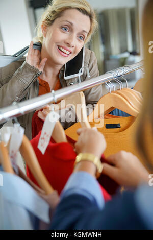 Mujer hablando por teléfono con un amigo, mientras que las compras en tienda de ropa Foto de stock