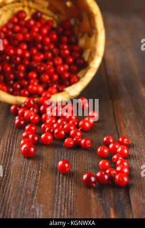 Cowberry, foxberry, arándano, Arándano rojo sorbos de la cesta sobre una tabla de madera marrón